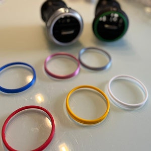 Könnte beinhalten: Eine Sammlung farbenfroher, kreisförmiger Ringe in Blau, Rot, Gelb, Weiß, Rosa und Grau. Im Hintergrund befinden sich zwei schwarze und silberne Geräte mit kreisförmigen Öffnungen. Die Ringe scheinen aus Kunststoff oder einem ähnlichen Material zu bestehen.