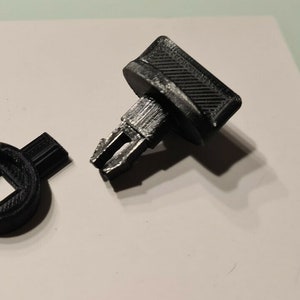 May include: A black plastic key with a square hole in the centre and a small metal pin. The key is broken into two pieces.