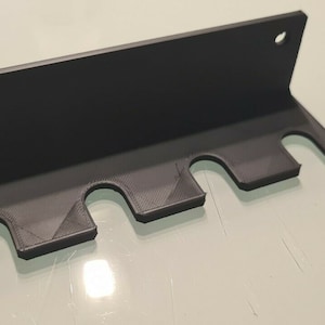 Peut inclure: Un support mural en plastique noir avec quatre crochets pour accrocher des outils ou d'autres objets. Le support a un trou pour le fixer à un mur.