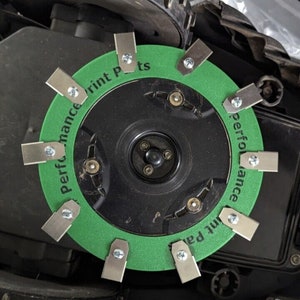 May include: Close-up of a green and black circular blade with the text "Performance Print Parts" around the edge. The blade is attached to a black robotic lawnmower.