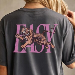 May include: Dark gray t-shirt with a pink tiger graphic and the text "EASY LADY". The tiger is orange and brown. The shirt is a short-sleeved, oversized style.