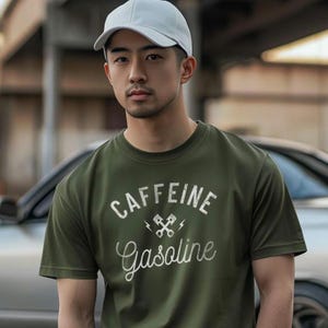 May include: A man wearing a green t-shirt with the text "Caffeine Gasoline" and a white cap. The shirt has a graphic of two crossed wrenches with lightning bolts.