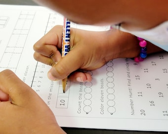 May include: A child's worksheet with a number line, a section to count beads, and a number hunt activity. The child is using a pencil to fill in the missing number on the number line.
