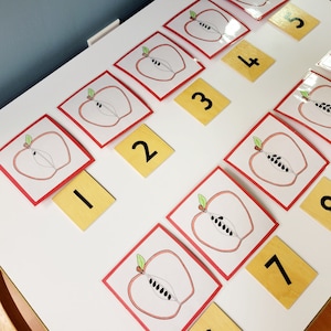 May include: A set of red and white cards with images of apples and numbers 1 to 10. The cards are arranged in a grid pattern on a white surface.
