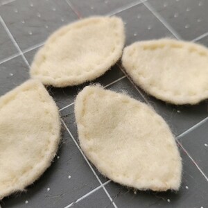 May include: Four off-white felt leaf shapes with a stitched edge.
