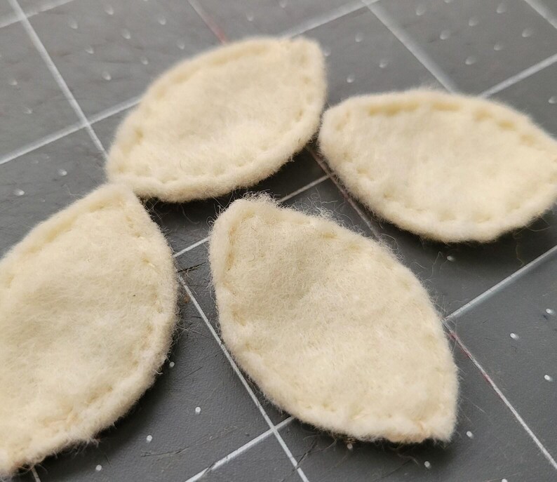 May include: Four off-white felt leaf shapes with a stitched edge.