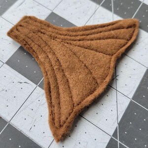 May include: A brown felt tail fin with a scalloped edge and stitched lines, resembling a fish tail.