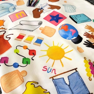 May include: A white fabric featuring a colorful repeating pattern of various illustrations including a yellow sun with the word sun written below it, a blue globe, spools of thread, wooden blocks, a pitcher, a chair, and hands in different skin tones.