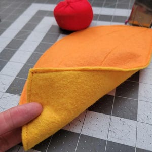 May include: A reversible fabric square with one side orange and the other side yellow. The fabric is folded in half to show both sides.