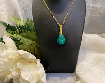 May include: A gold chain necklace with a teardrop-shaped pendant made of green resin with iridescent glitter.