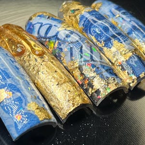 May include: Five blue and gold nail tips with a dollar bill design. The tips are curved and have a glossy finish.