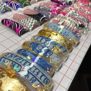 May include: A set of false nails with various designs, including a zebra print, a Union Jack flag, and a design featuring gold leaf and a US dollar bill.