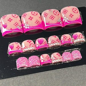 Puede incluir: Un juego de uñas postizas con base nude, estampado de monograma rosa, puntas francesas de color rosa brillante, pequeños diamantes de imitación transparentes y corazones rosas. Incluye varios tamaños, con algunas uñas cubiertas de purpurina.