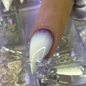 May include: A stiletto-shaped artificial fingernail featuring a smooth gradient transition from a deep purple base near the cuticle to a solid white tip, accented with a small, sharp, silver-colored metal spike detail near the end.