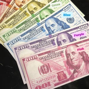 May include: A stack of $100 bills, each one a different color of the rainbow, starting with red and ending with pink. The bills are arranged in a fan shape, with the red bill at the top and the pink bill at the bottom.