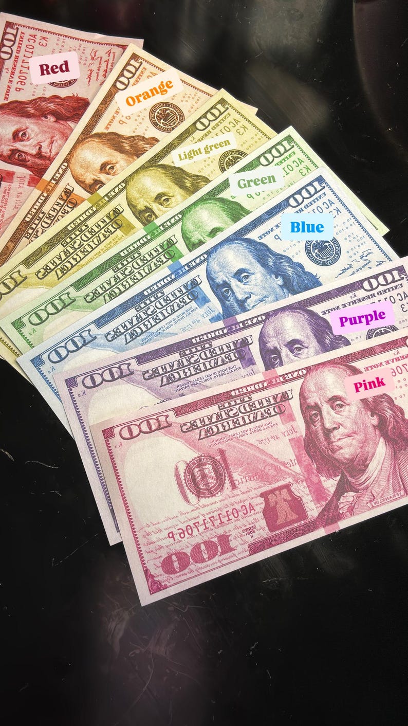 May include: A stack of $100 bills, each one a different color of the rainbow, starting with red and ending with pink. The bills are arranged in a fan shape, with the red bill at the top and the pink bill at the bottom.