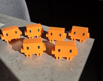 May include: Six orange, pixelated creature figurines with black square eyes and small legs are arranged on a grey surface. The figurines are evenly spaced and appear to be 3D-printed. The background is blurred, with a dark silhouette.