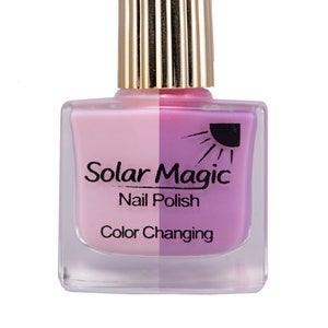 May include: A clear glass bottle of Solar Magic color changing nail polish. The bottle has a gold cap and a pink and purple liquid inside.