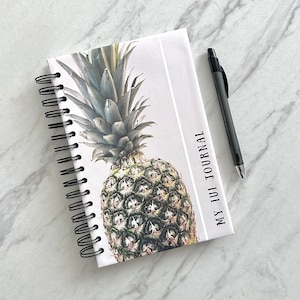 May include: A spiral bound journal with a white cover and a pineapple illustration. The cover text reads "My Iui Journal".