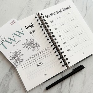 Puede incluir: Un diario de espera de dos semanas con un dise&ntilde;o de pi&ntilde;a en blanco y negro en la portada. El diario tiene una encuadernaci&oacute;n en espiral e incluye secciones para registrar fechas, s&iacute;ntomas, emociones y notas. El texto "The TWW (Two Week Wait)" est&aacute; impreso en una tarjeta separada.