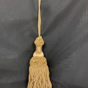 May include: A gold tassel with a long cord. The tassel is made of twisted threads and has a decorative knot at the top.