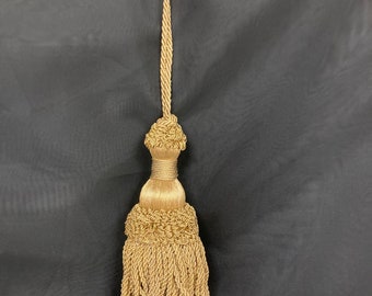 May include: A gold tassel with a long cord. The tassel is made of twisted threads and has a decorative knot at the top.