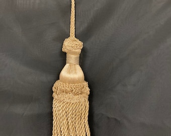 May include: A gold tassel with a long, twisted cord. The tassel has a decorative knot at the top and a fringe at the bottom.