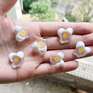 Puede incluir: Seis pequeños amuletos de plástico transparente en forma de huevo con una yema de huevo amarilla en el interior. Los amuletos están partidos para revelar la yema.