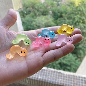 May include: Six colorful gummy worm charms with smiling faces. The worms are in various colors, including pink, blue, green, yellow, and light blue.