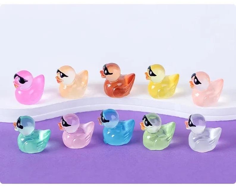 May include: A set of ten colorful rubber duck toys with sunglasses. The ducks are in various colors, including pink, yellow, blue, green, and clear. Each duck has a black pair of sunglasses.