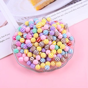 May include: A bowl filled with colorful striped candy balls. The candy balls are a mix of pink, yellow, blue, green, purple, and brown.