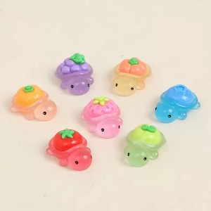 May include: A collection of colorful, miniature turtle figurines. Each turtle has a different fruit or vegetable on its back, including grapes, strawberries, and tomatoes. The turtles are in shades of pink, orange, green, and blue.