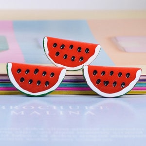 Könnte beinhalten: Drei rote Wassermelonen-Scheiben-Anhänger mit schwarzen Kernen und weißen und grünen Umrissen.