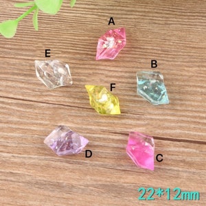 May include: Six colourful, faceted, diamond-shaped resin embellishments with gold glitter. The embellishments are approximately 22mm by 12mm. The colours are pink, light blue, purple, pink, clear, and yellow.