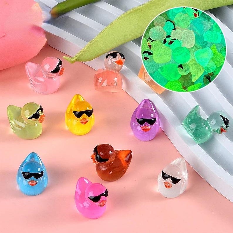 May include: A collection of ten colorful rubber duck toys with sunglasses. The ducks are in various colors, including yellow, blue, pink, green, and purple. The ducks are all wearing sunglasses and have a rubbery texture.