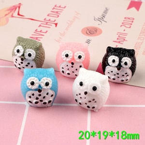 Pode incluir: Cinco miniaturas de coruja em diferentes cores: verde, rosa, azul, branco e preto. Cada coruja tem olhos pretos e um bico branco. As corujas medem aproximadamente 20 mm x 19 mm x 18 mm.
