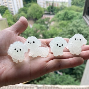 May include: Four small white fluffy dog figurines with black eyes. The figurines are made of a soft, squishy material and are about 5 cm tall.