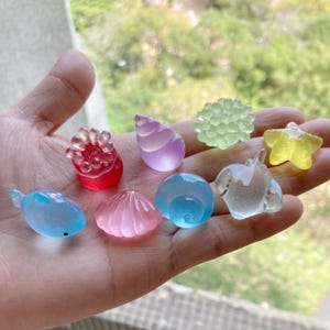 May include: A collection of nine colorful resin sea life charms, including a starfish, a seashell, a coral, a seahorse, and a sea urchin. The charms are translucent and have a glossy finish.
