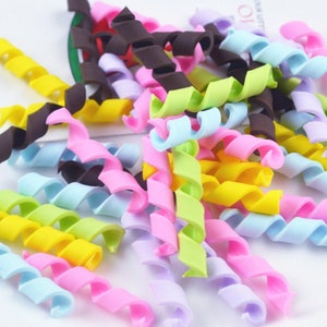 May include: A collection of colorful, curly, plastic pipe cleaners in various pastel shades, including pink, blue, yellow, and green. The pipe cleaners are arranged in a random pile on a white surface.