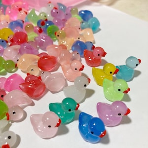Könnte beinhalten: Eine Sammlung bunter Glas-Entenfiguren. Die Enten sind in verschiedenen Schattierungen von Rosa, Blau, Grün, Gelb und Weiß. Sie sind alle klein und haben eine glänzende Oberfläche.