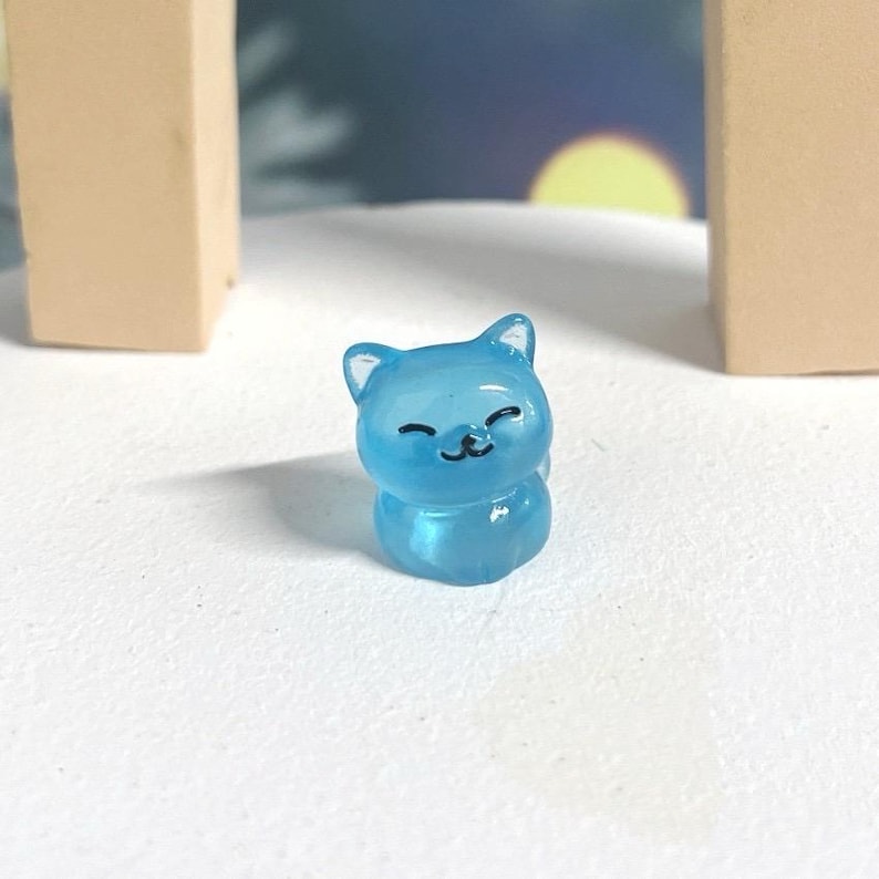 May include: A small, light blue, translucent cat figurine with a smiling face. The figurine is made of plastic and has a glossy finish.