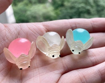 May include: Three small, translucent, bug-shaped toys with round bodies and black eyes. The toys are made of a clear plastic material and are filled with colored liquid. The colors of the liquid are pink, white, and blue.