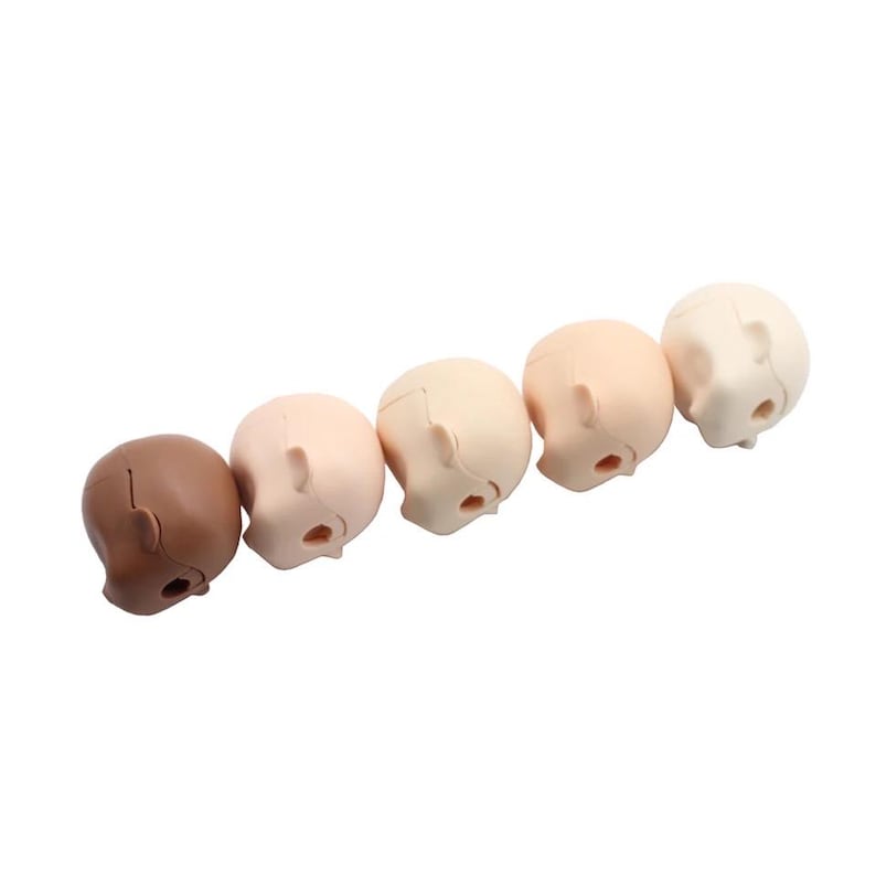 May include: Six doll heads in various skin tones, all facing down. The heads are made of a smooth, light-colored plastic.