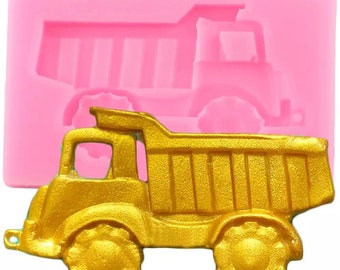 Puede incluir: Un molde de silicona rosa para hacer un camión de volteo de juguete de color dorado. El molde tiene la forma de un camión de volteo con un diseño en relieve.