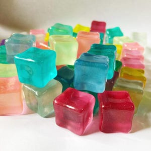 Könnte beinhalten: Eine Sammlung von bunten, durchsichtigen, würfelförmigen Eiswürfeln. Die Würfel bestehen aus einem klaren Material und haben eine Vielzahl von Farben, darunter Blau, Grün, Pink, Gelb und Orange.