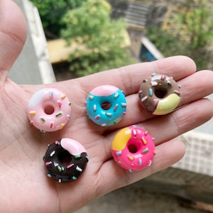 以下が含まれることがあります： 異なる色の釉薬とスプリンクルをかけたミニドーナツ5個。ドーナツはピンク、ブルー、イエロー、ブラウン、ホワイトです。