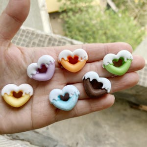 May include: Six heart-shaped donut charms in various colors, including purple, orange, green, brown, blue, and yellow. The charms are made of polymer clay and have a glazed finish.