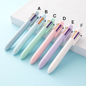 May include: Six multi-colored ballpoint pens with different colored barrels. The pens are arranged in a row from left to right, with the darkest color on the left and the lightest color on the right. The colors are: light blue, light green, pink, purple, white, and light blue.