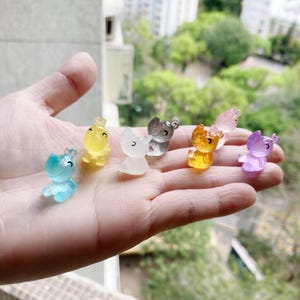 May include: A set of seven small, colorful, animal figurines. The figurines are made of clear plastic and have a glossy finish. The animals include a blue hippo, a yellow unicorn, a white unicorn, a gray unicorn, a yellow unicorn, a purple unicorn, and a pink unicorn.