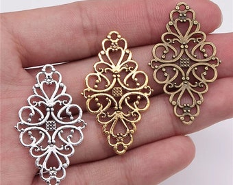 May include: Three filigree metal pendants in silver, gold, and bronze. Each pendant has an ornate, openwork design with heart and scroll details. The pendants are diamond-shaped with a square accent in the center.